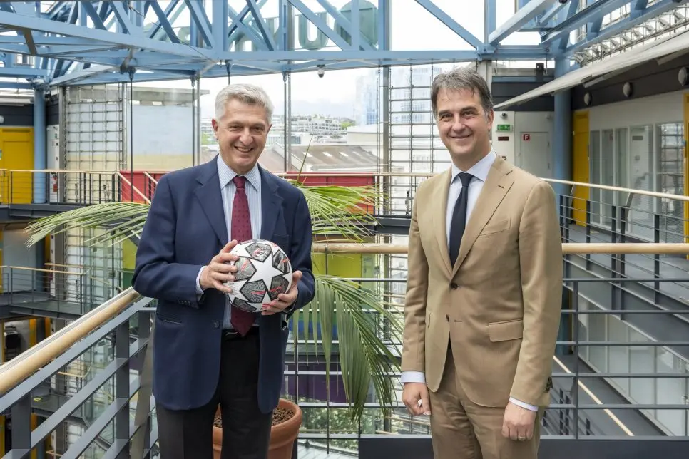 Two men pose while holding a soccer ball.