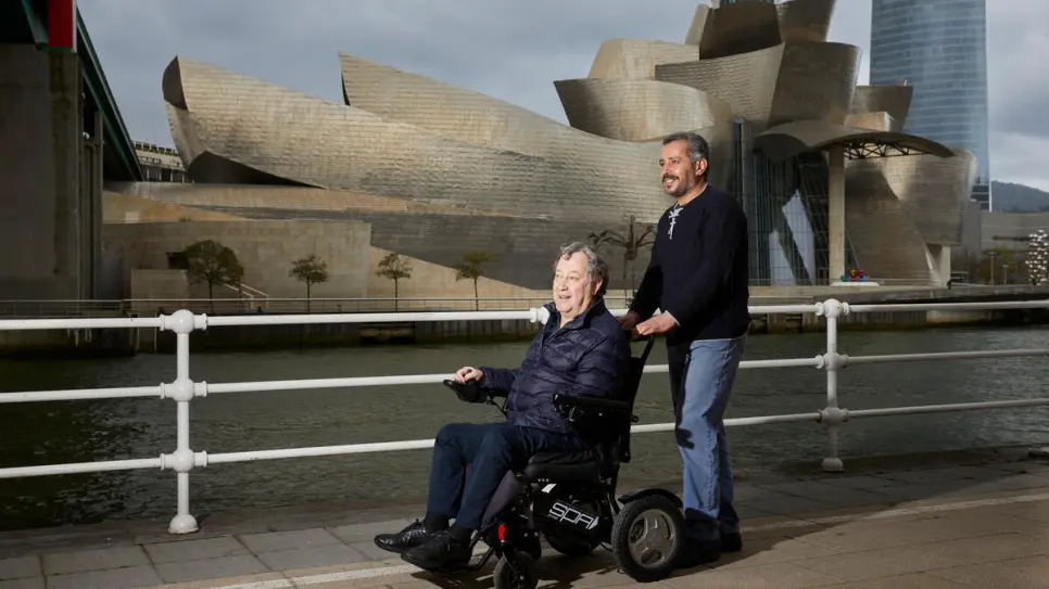 Man pushes another man in wheelchair.