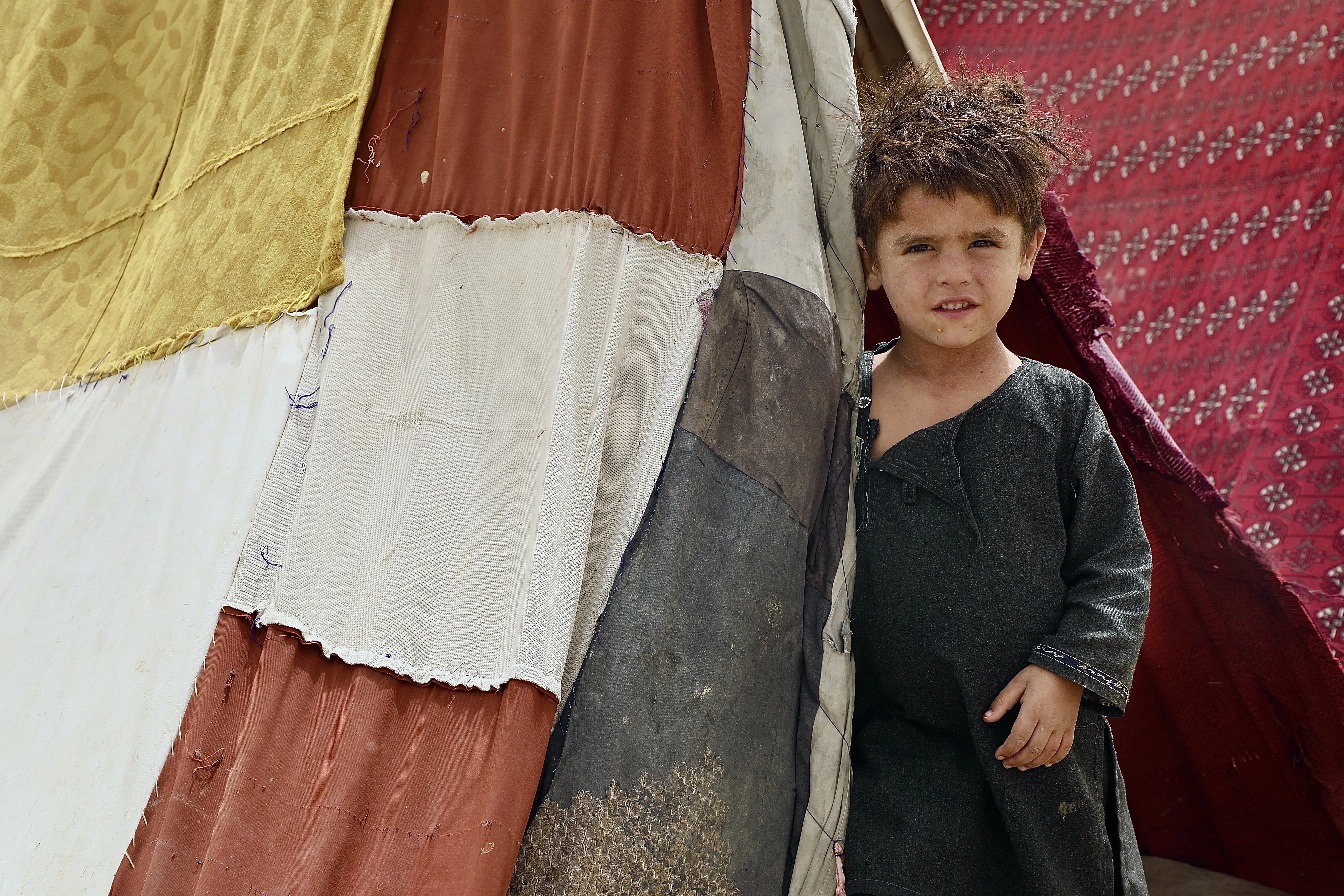 Zarif, 6 stands peaks from his grandmother, Herati’s makeshift tent. His father was killed during the clashes between the government and the non-government armed forces