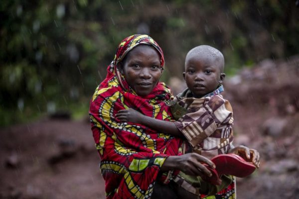 Woman in multicoloured covering holds small child in rain