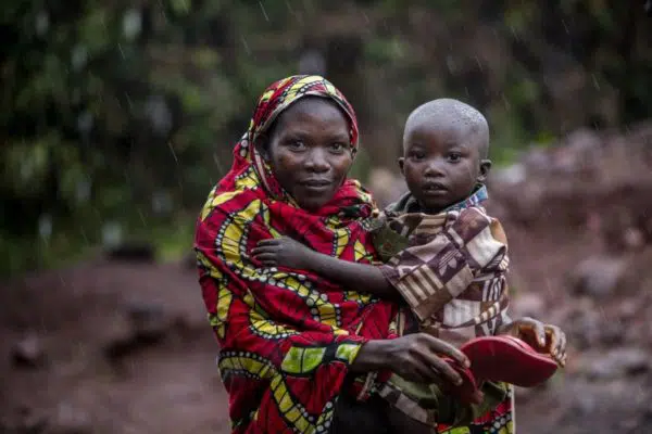 Woman in multicoloured covering holds small child in rain