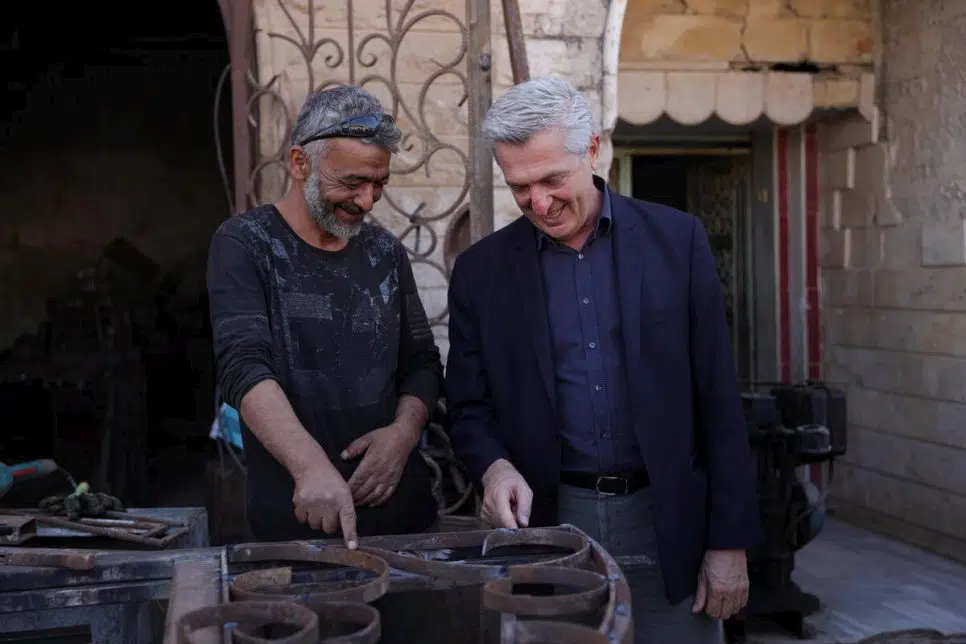 Blacksmith Wasel points to iron piece standing next to UN High Commissioner for Refugees Filippo Grandi