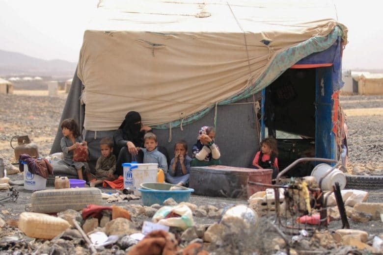 Children sitting outside a tent surrounded by rubble.