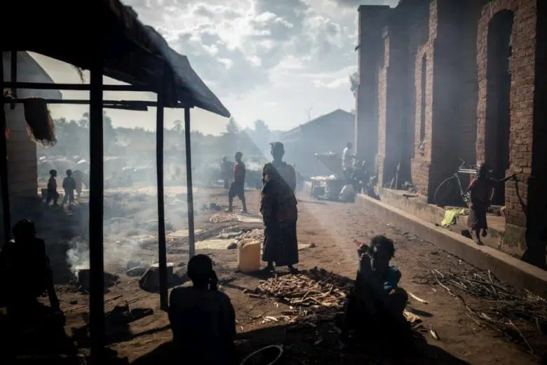 Woman standing with people sitting on a dirt road.