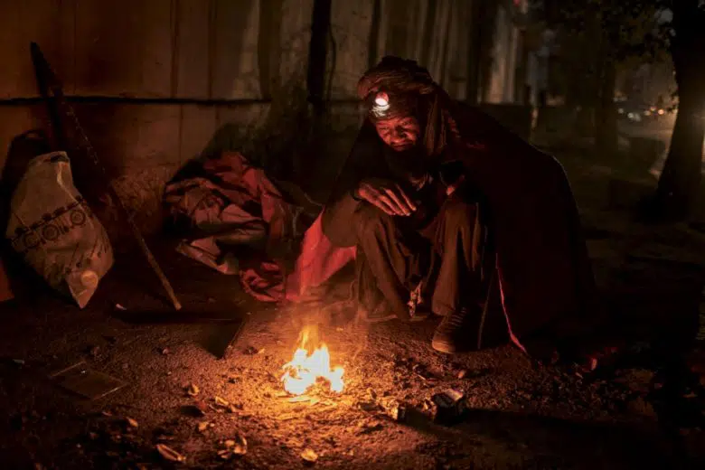 A man is sitting near a makeshift fire pit.