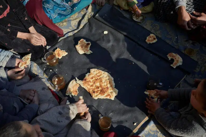 A displaced family of nine share a piece of bread for their midday meal
