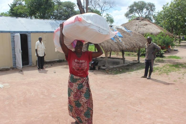 Woman carrying supplies in a large bag above her head.