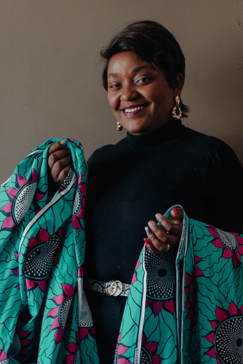 Dark skinned woman with a short pixie cut wearing black long sleeved turtle neck shirt and bold gold earrings, holds turquoise fabric with magenta and black flower patterns on it.