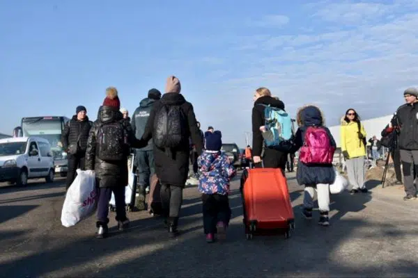 The backs of women and children holding hands as they drag their suitcase behind them.