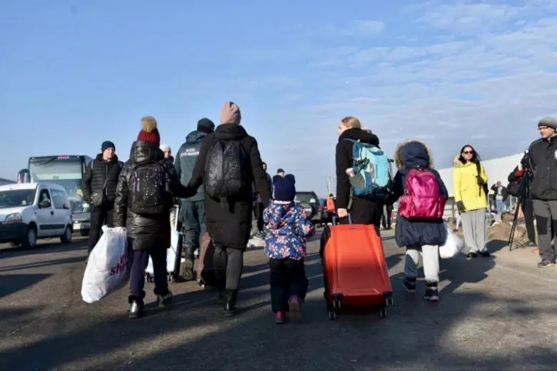 The backs of women and children holding hands as they drag their suitcase behind them.