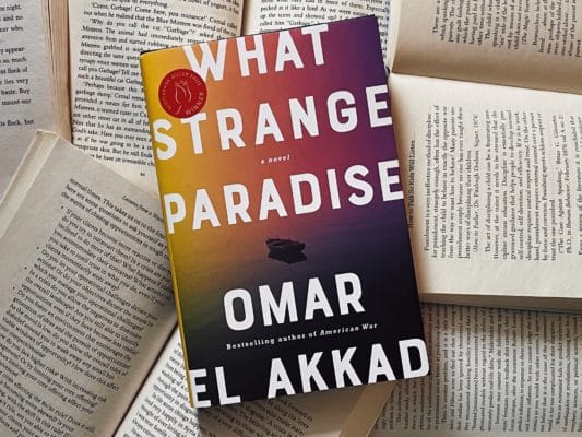 The novel "What Strange Paradise" placed on top of open books.