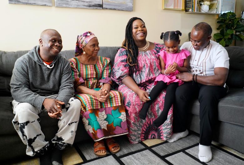 From left to right: Elijah Gboeah, Martha Gboeah, Lourena Gboeah, Moriah Flomo, and Jonah Flomo seated on grey couch with beige wall behind