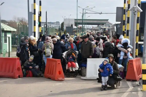 Group of people at a border crossing with orange and white street blockages. There is a child and his mother in front.