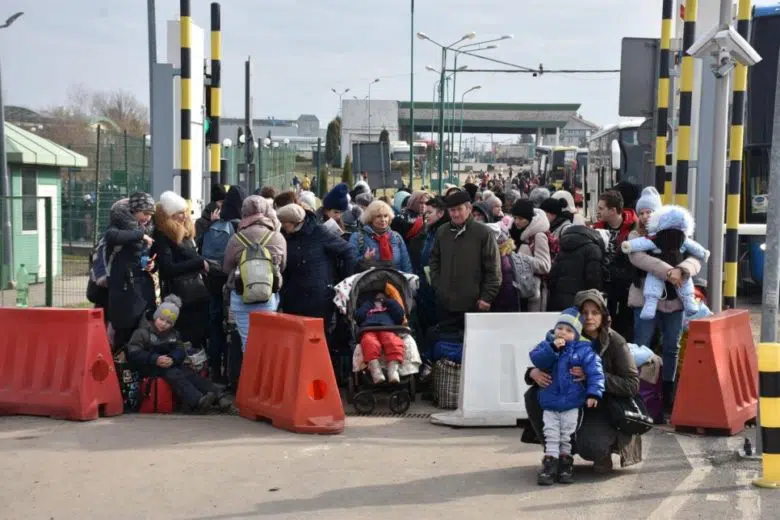 Group of people at a border crossing with orange and white street blockages. There is a child