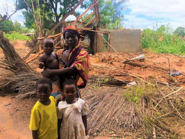 Famille regardant la caméra, derrière eux se trouve une maison détruite.