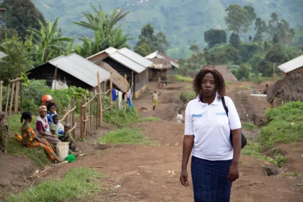 Lidia in the foreground wearing a white UNHCR tshirt with the village behind her