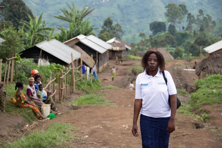 Lidia in the foreground wearing a white UNHCR tshirt with the village behind her
