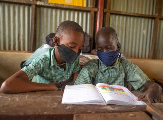 Two children share a textbook in a classroom.