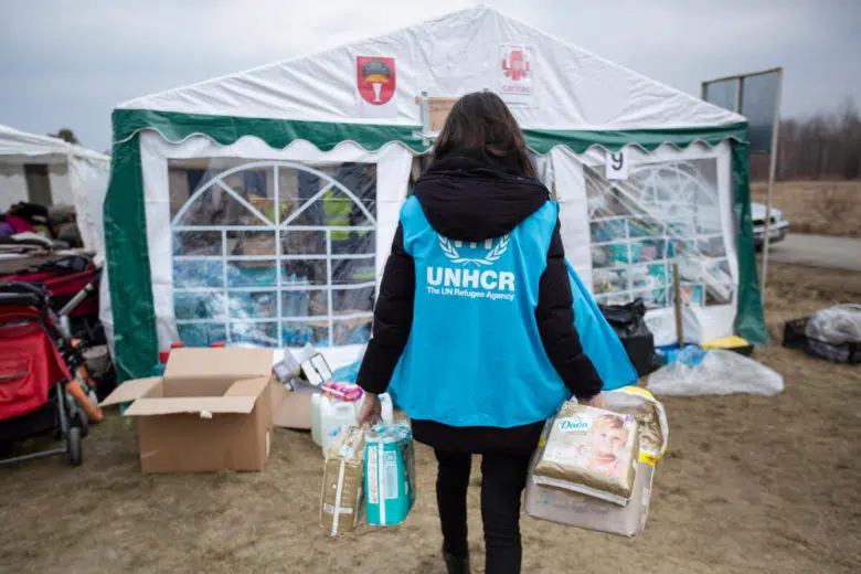 Female UNHCR employee carrying supplies into large white tent
