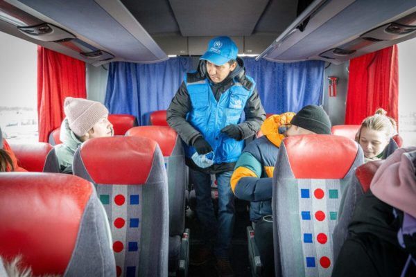 Un employé du HCR avec une casquette bleue surveillant un bus avec des réfugiés ukrainiens.