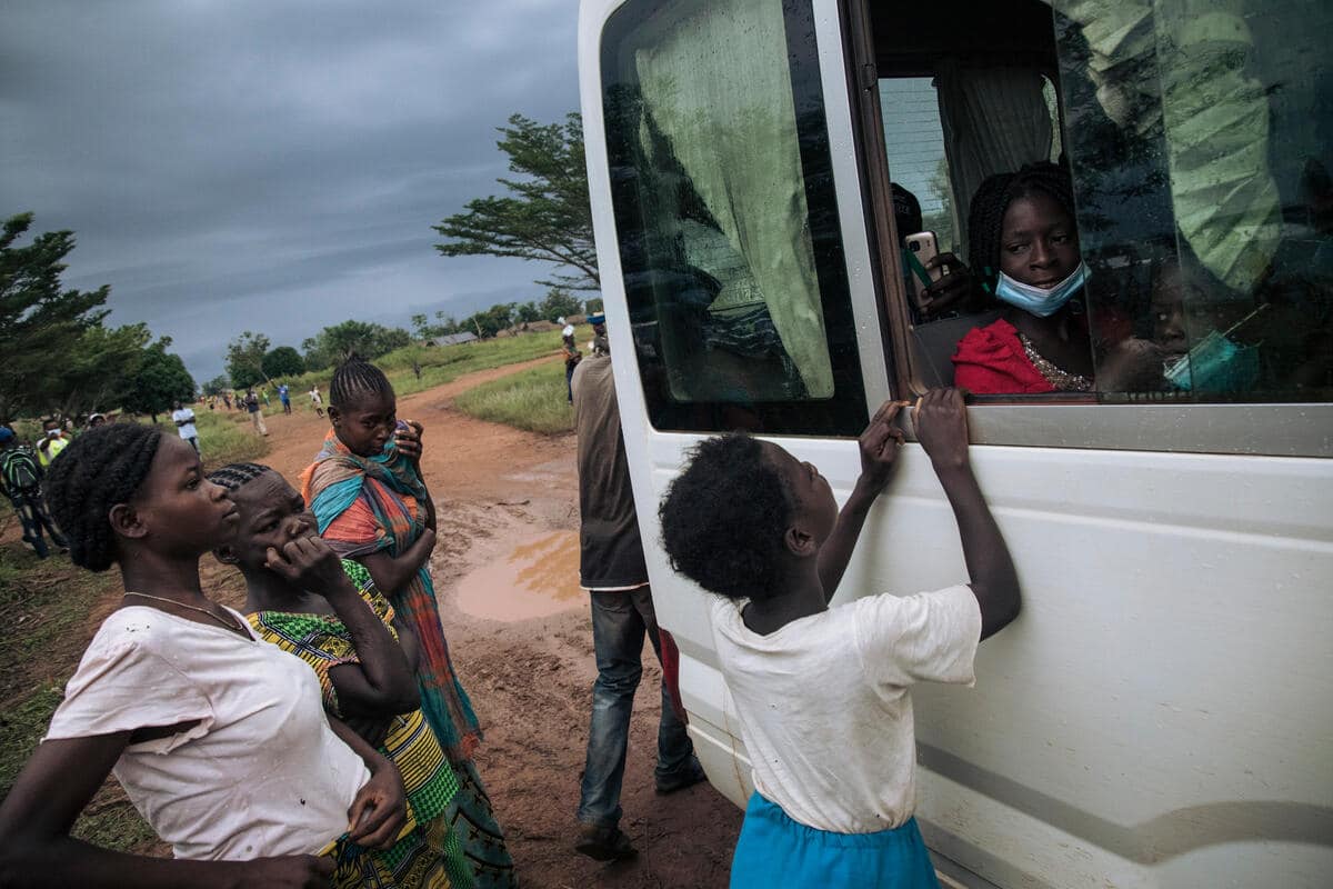 Congolese refugees standing outside the window of a white van with a young relative sitting on the inside at the open window