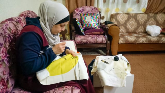Woman wearing a grey hijab sewing an off-white pillow case with a large yellow circle