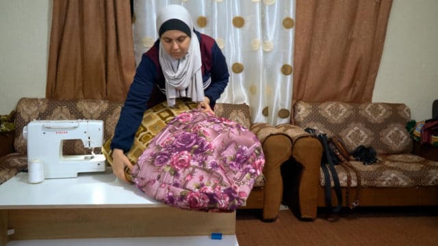 Woman wearing a grey hijab putting a purple floral pillow covering on a couch pillow