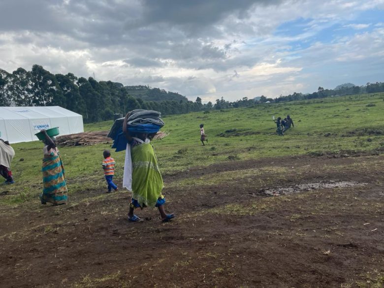 People walking with supplies of blankets and buckets across muddy fields.