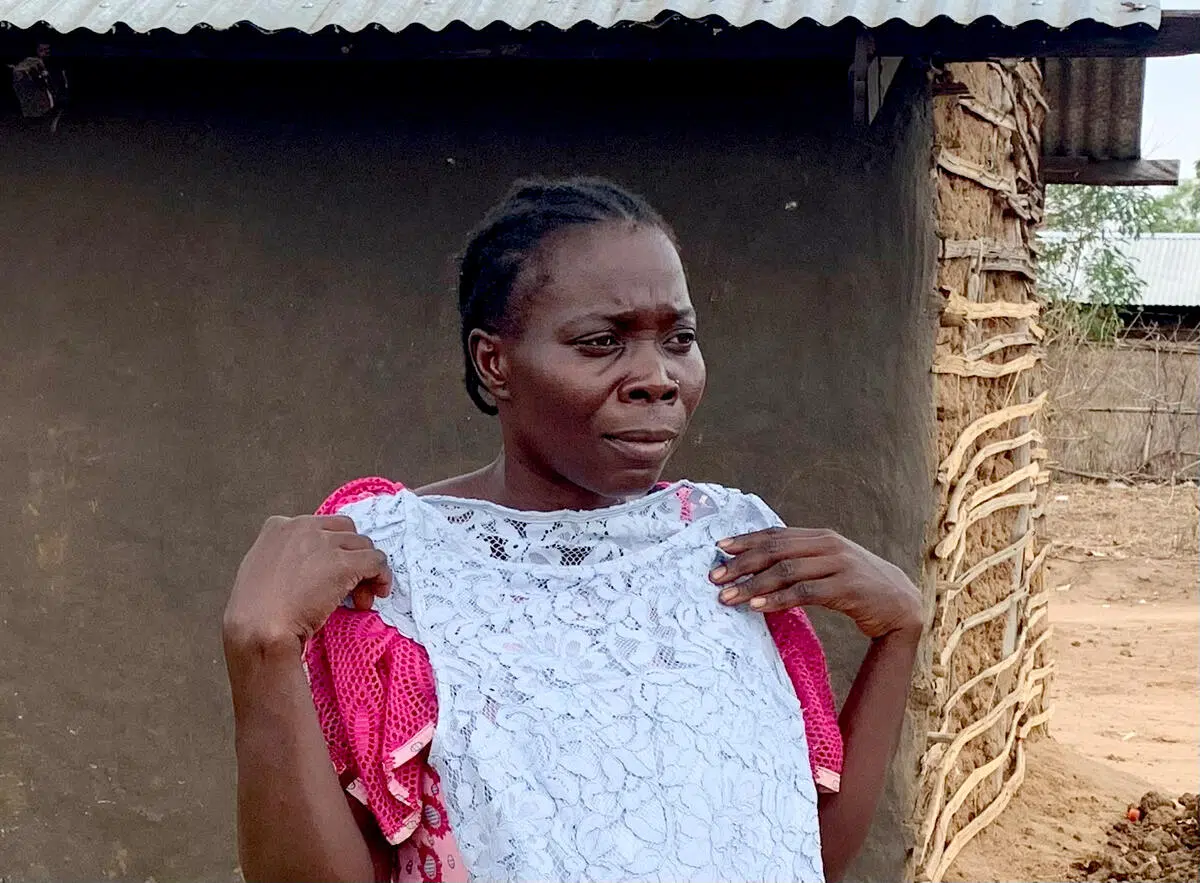 woman wearing pink dress holding up a white lace dress against her body, she is standing in front of a brown clay building