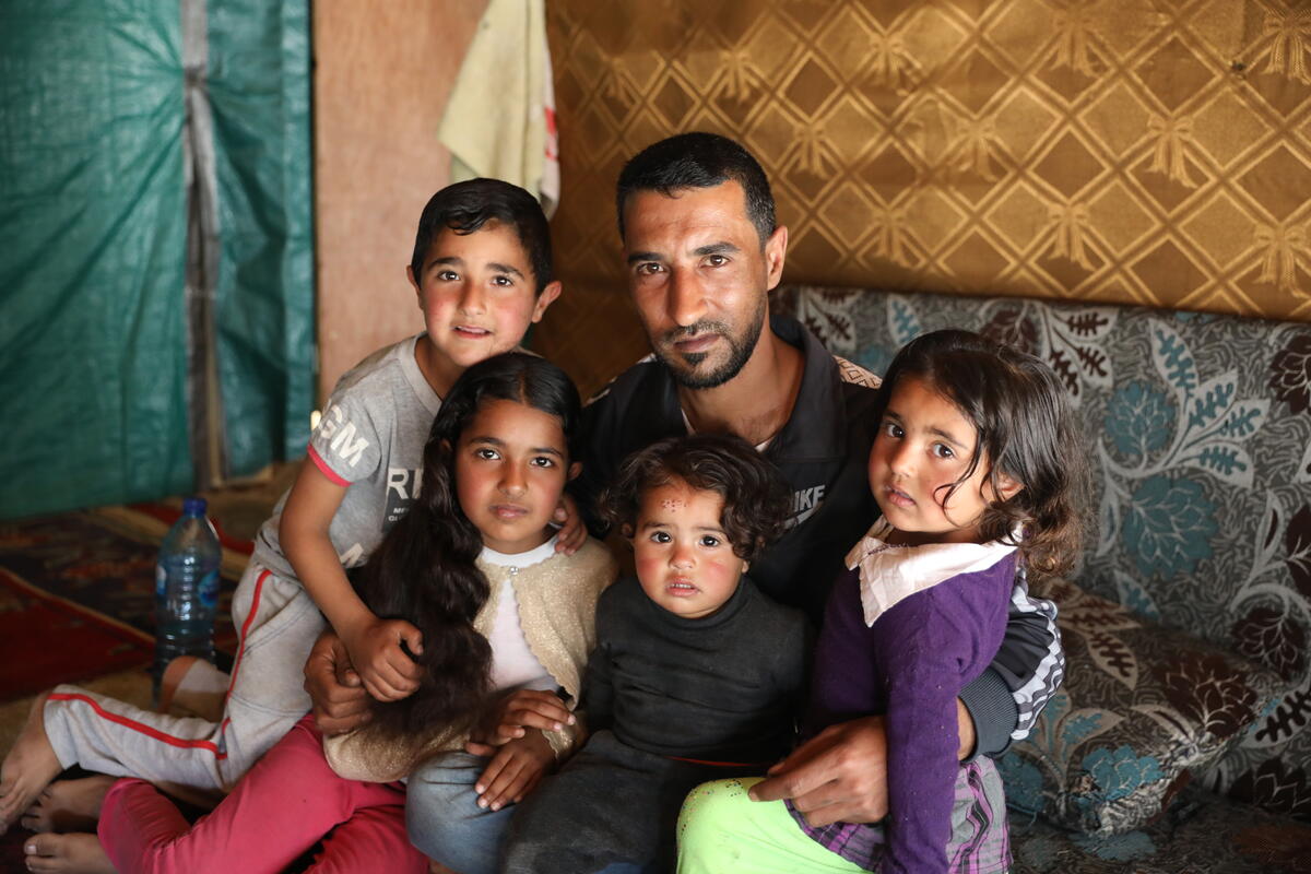 Syrian father sitting with his four young children in his arms 