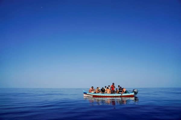 Small boat filled with people, all wearing life jackets, in the middle of the ocean