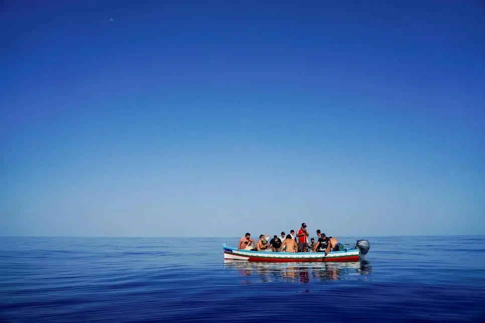 Small boat filled with people, all wearing life jackets, in the middle of the ocean