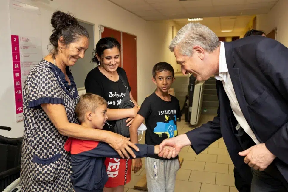 Man wearing suit leaning down to shake the hand of a young boy who is standing in front of two smiling women and another young boy