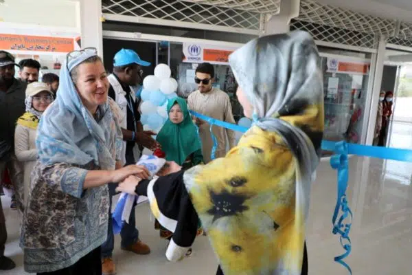 Two women facing each other holding hands in front of a blue ribbon that goes width wise across the room