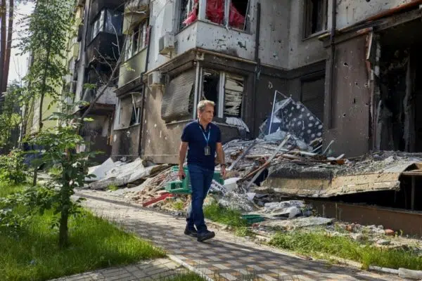 man walking alone stone path in front of run down building, he is wearing a dark blue polo shirt and blue jeans