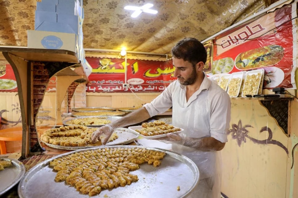 Arab man plating various puff pastries on a silver tray in a shop with red walls