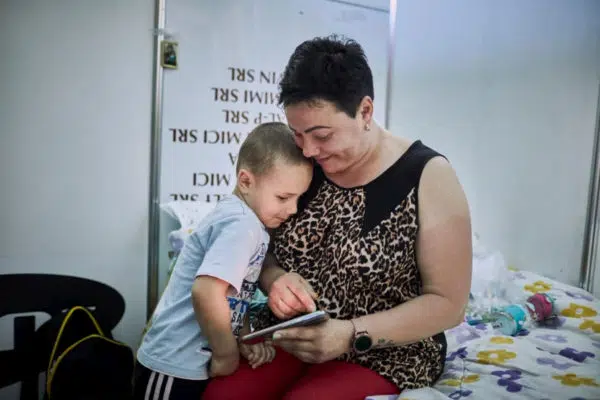 Woman wearing a leopard print, short-sleeve, shirt sitting with a young boy who is leaning into her