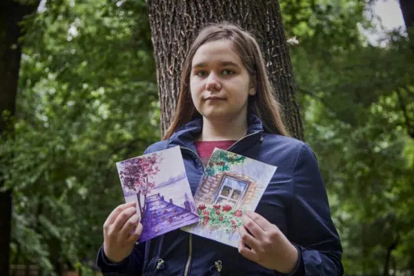 young woman holding up two small paintings