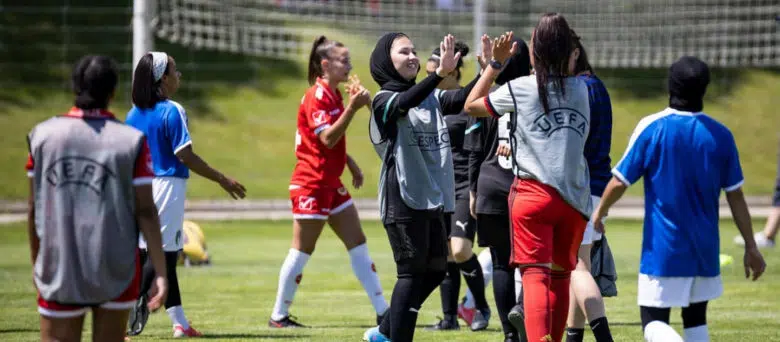 young women in soccer gear on the field, two are centre frame giving each other a high five