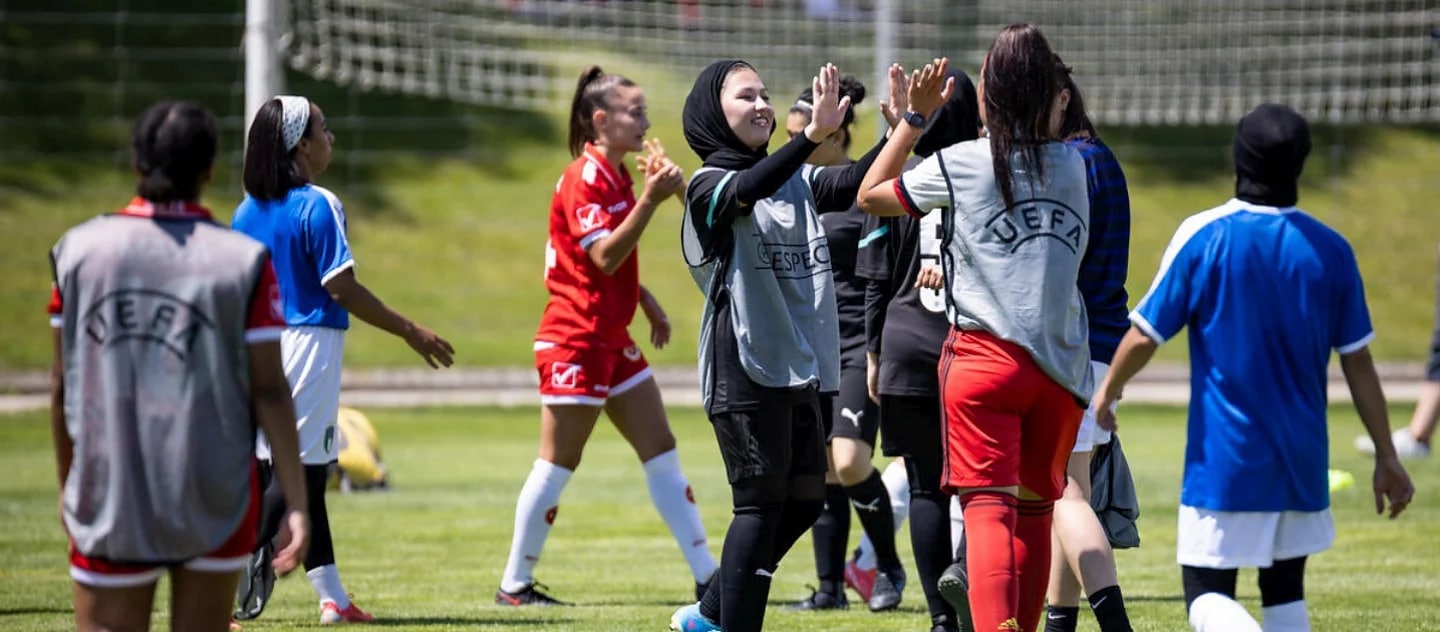 young women in soccer gear on the field, two are centre frame giving each other a high five 