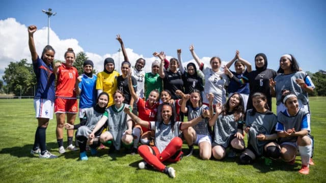 Group of female soccer players posing for a team photo with their arms in the air expressing excitment