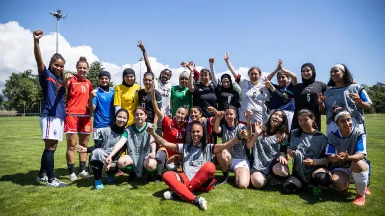 Group of female soccer players posing for a team photo with their arms in the air expressing excitment