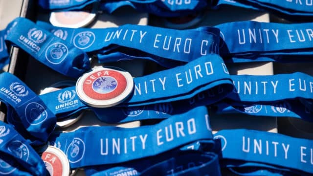 pile of medals with blue ribbons, the medal reads "UEFA" while the ribbons depict the UNHCR logo and read "Unity Euro"
