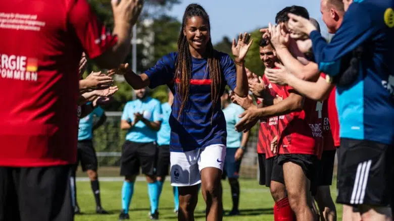 woman wearing a dark blue soccer jersey and white soccer shorts is walking through a crowd smiling and giving everyone a high five