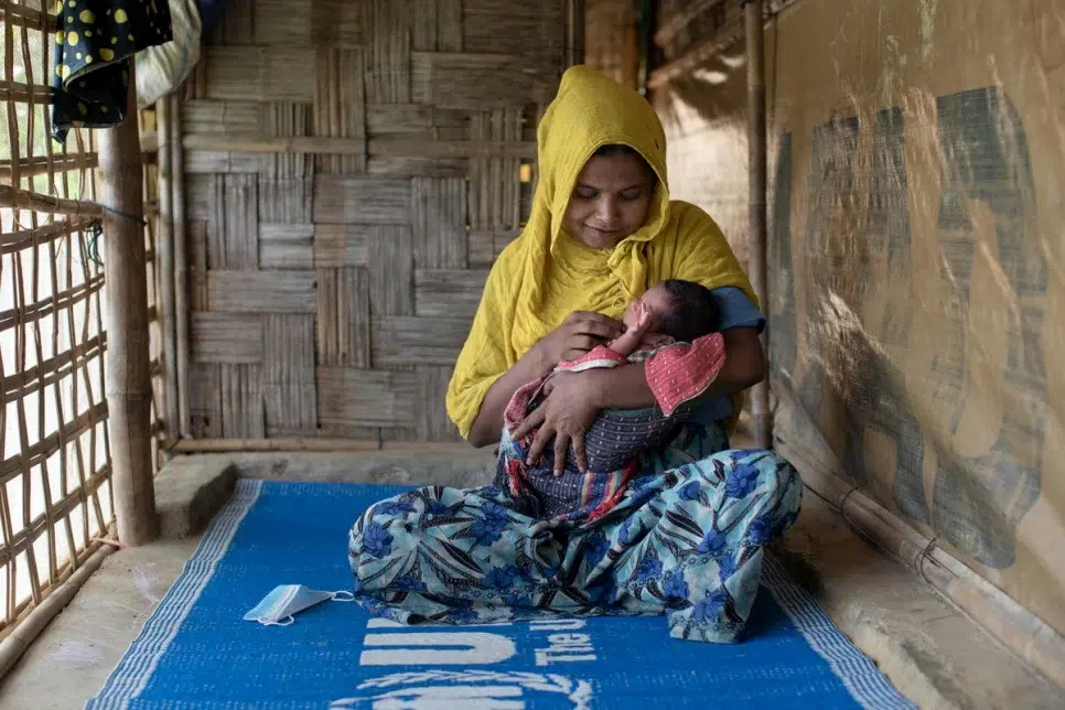 Woman in yellow head scarf and blue floral patterned dress looking down cradling her newborn in her arms.