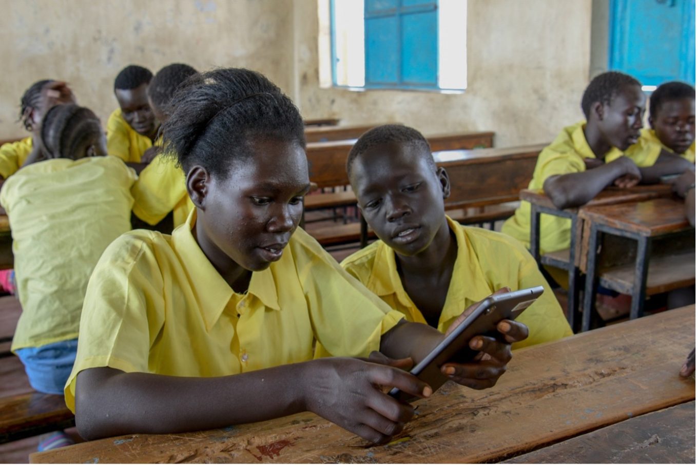 Youth in yellow school uniform sitting at desk looking at smartphone.