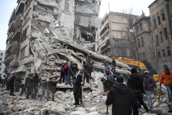 Collapsed building with rubble at the base. There are people