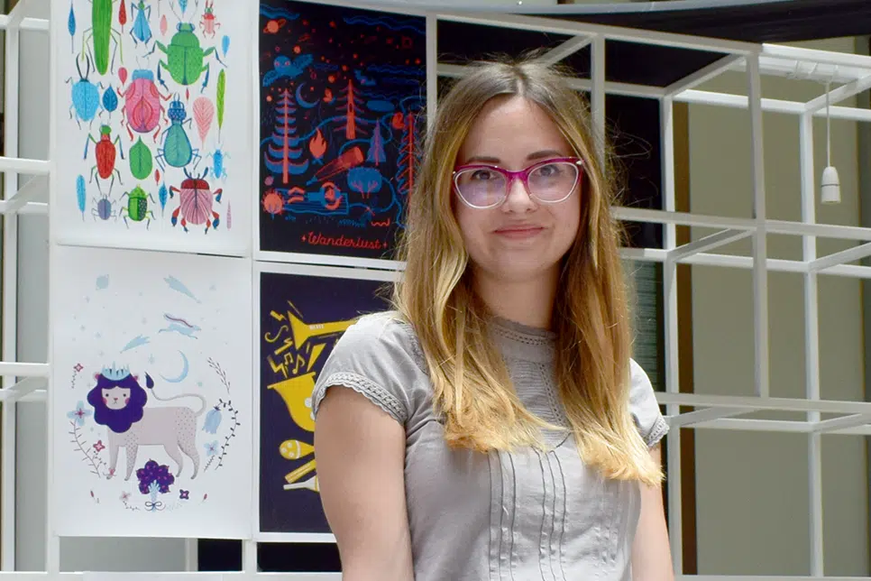 Woman stands in front of white shelves with four art prints hanging on display.