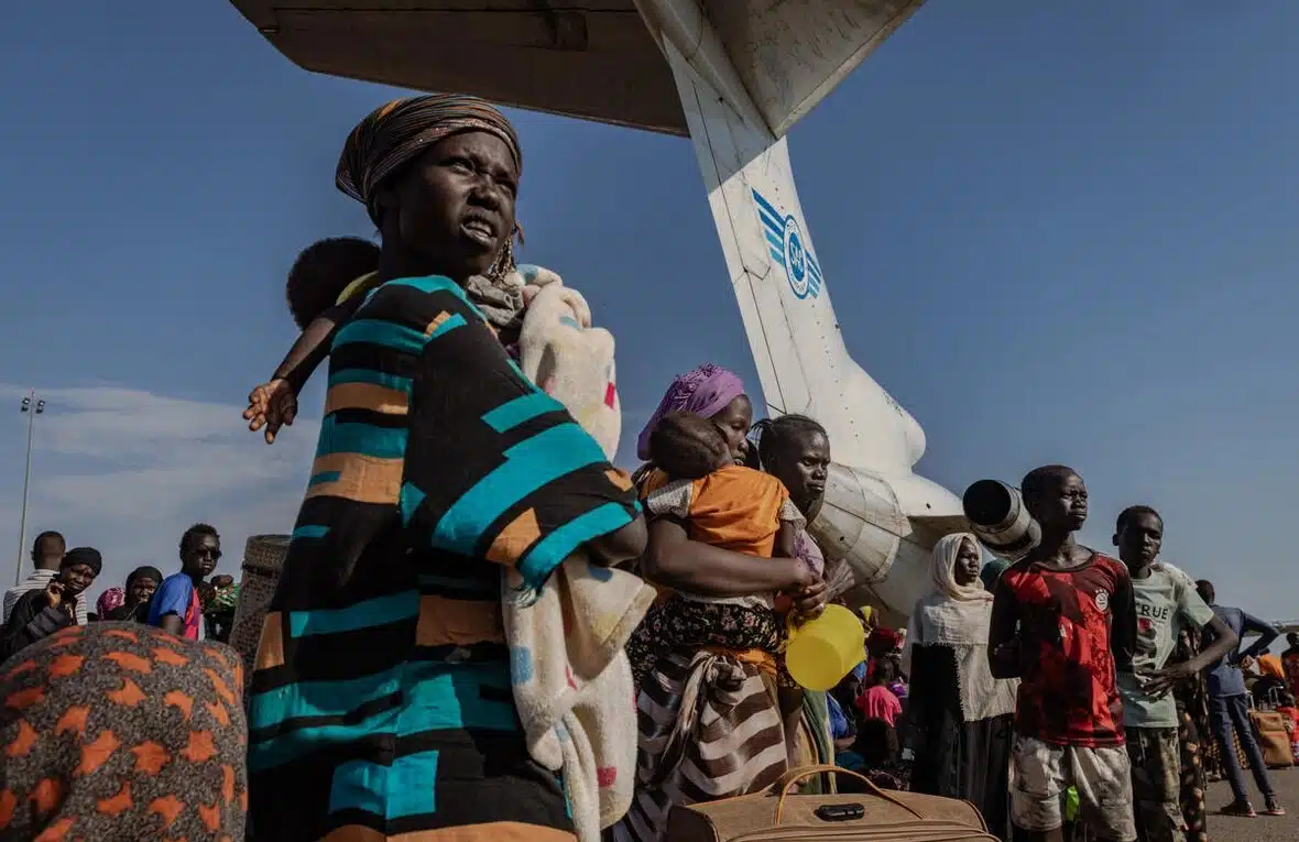 A woman holding a child in front of a crowd and airplane.