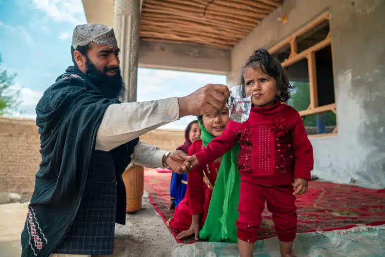 Man hold glass of water to child's mouth.